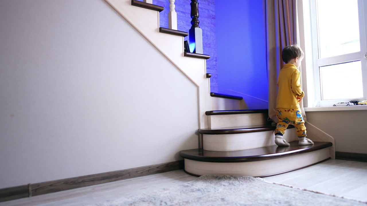 Lovely toddler in yellow clothes stepping cheerfully by the stairs. Cute child looks into the window.