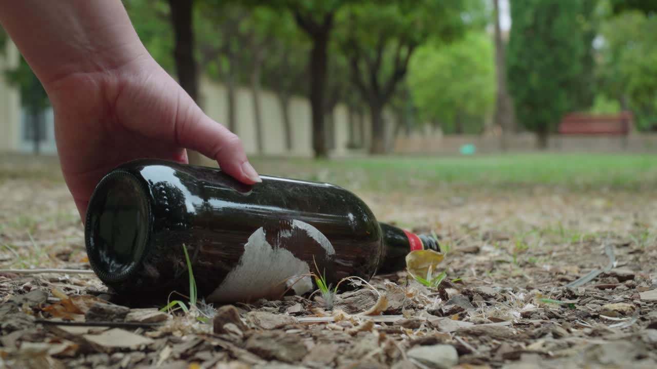 recogiendo a mano una botella de cerveza llena de basura con una bebida derramándose en el parque, cerrada