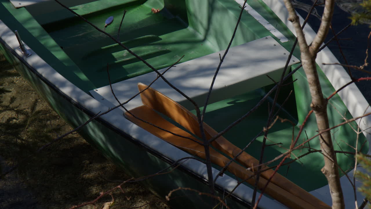 Wooden Boat With Paddles Resting On The Lakeshore. High Angle Shot