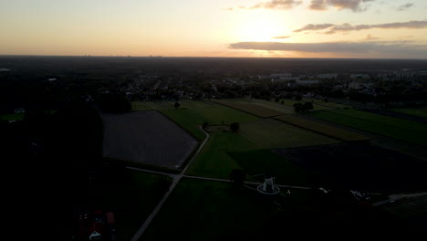 Aerial-of-classic-windmill-surrounded-by-green-meadows-at-sunset---drone-flying-backwards