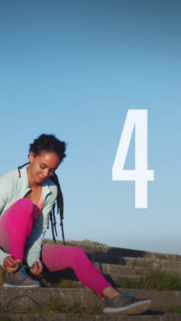 Number-countdown-against-african-american-fit-woman-tying-her-shoe-laces-sitting-on-the-stairs