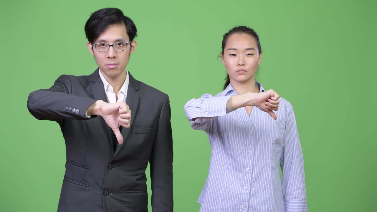 Young Asian business couple giving thumbs down together