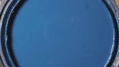 cerca de una mujer abriendo una lata de pintura de acero para revelar pintura azul.