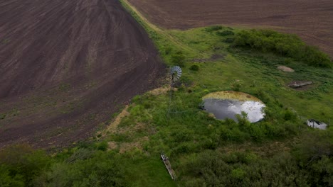 Aerial-pan-of-windmill-water-pump-in-rural-green-landscape,-Argentina