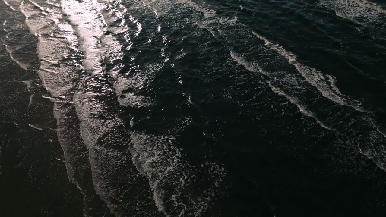 Aerial drone footage of the sea capturing abstract patterns of waves illuminated by backlight