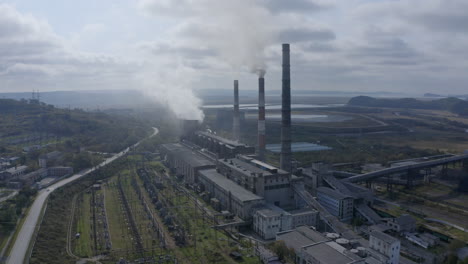 Slow-pivot-shot-of-a-coal-fired-power-station-with-its-chimneys-and-funnels-releasing-white-smoke-into-the-air-on-a-sunny-and-cloudy-day