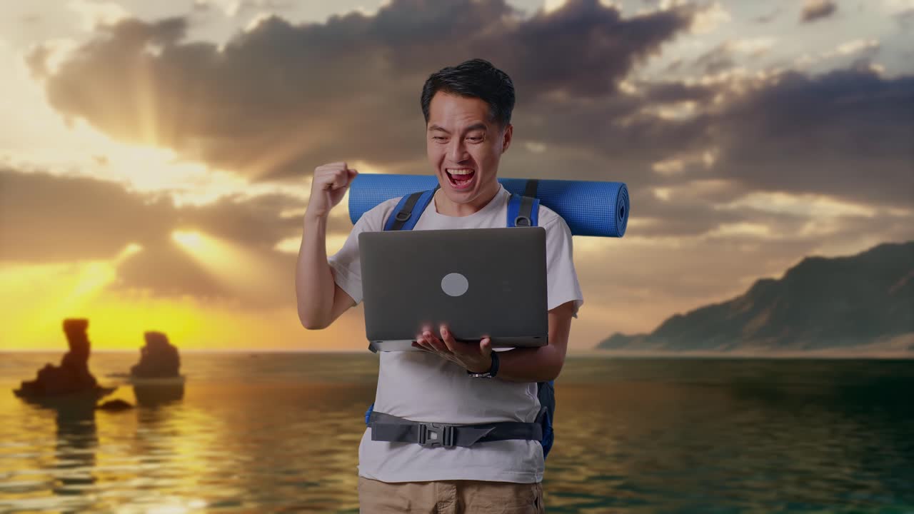 Aziatische mannelijke wandelaar met bergbeklimmersrugzak die naar een laptop kijkt en juichend zijn succes viert op het strand