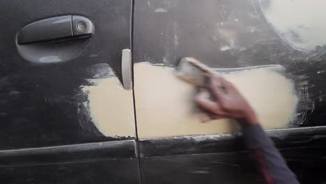 a worker rubbing car metal lambi putty on car