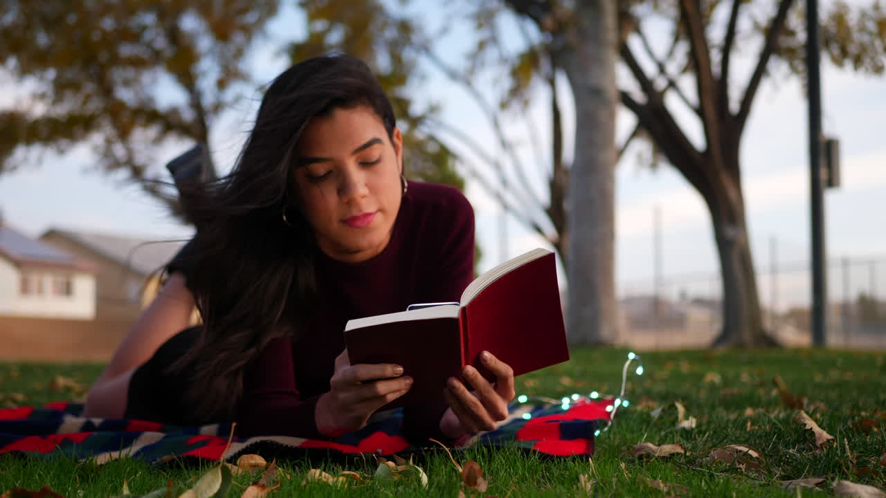 una hermosa joven hispana abriendo las páginas de un libro de cuentos o novela y leyendo en el parque en otoño deslice hacia la derecha