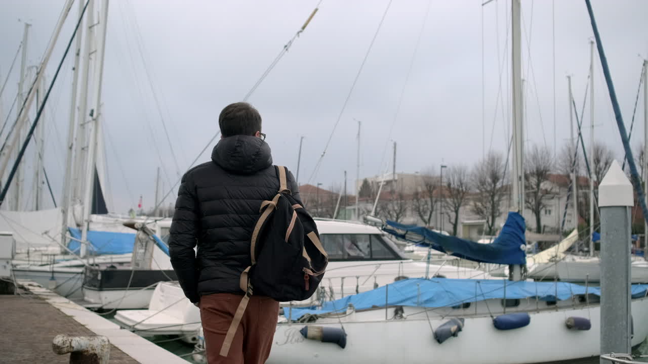 Mann geht an einem Hafendock mit Yachten entlang