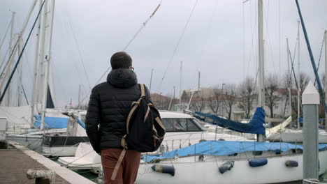 man walking along a waterfront dock with yachts