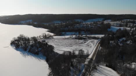 Aerial-flyover-beautiful-winter-landscape-with-snow-covered-farm-fields-and-forest-trees-in-Sweden