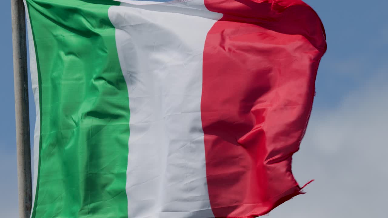 Italian tricolor flag waves dynamically on flagpole outdoors, bright daylight, clear blue sky background
