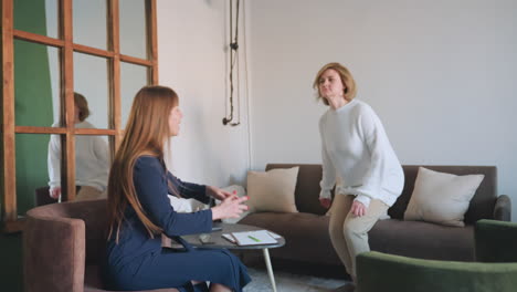 inspirer with warm smile gestures toward sofa while welcoming patient into comfortable lounge for supportive conversation, soft cushions and calm setting enhance experience