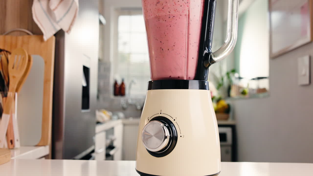 Blender, der mixer en sund, lyserød frugtsmoothie i et moderne køkken