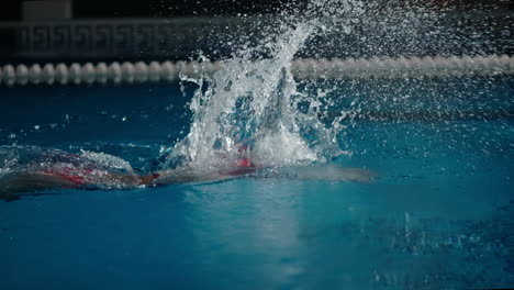a swimmer in a red swim cap and goggles does the butterfly stroke in a pool.