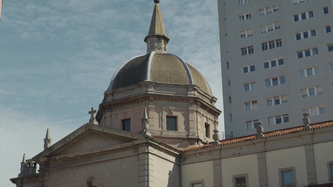 Antigo edifício religioso contrastando com um bloco de apartamentos moderno na cidade de Gijón, Astúrias