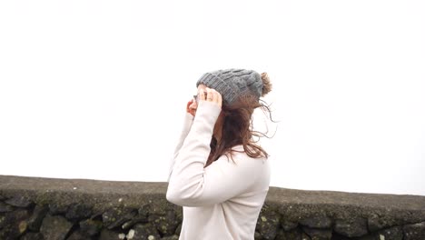 profile shot of woman on a windy day adjusting beanie in azores by sea wall