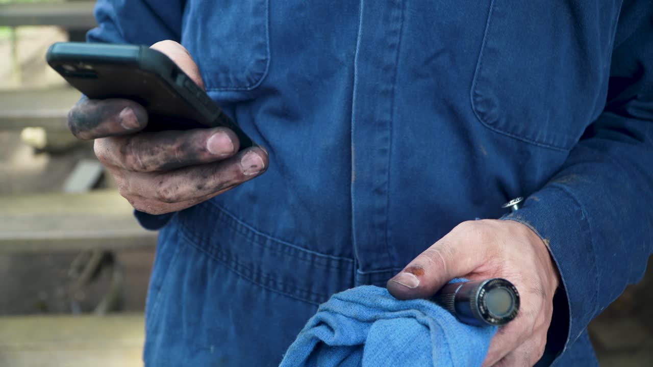 Primo piano di un uomo in tuta da lavoro con le mani sporche che usa il telefono cellulare per accedere a informazioni