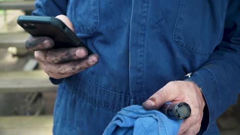 close up of man in coveralls with dirty hands using mobile phone to access information
