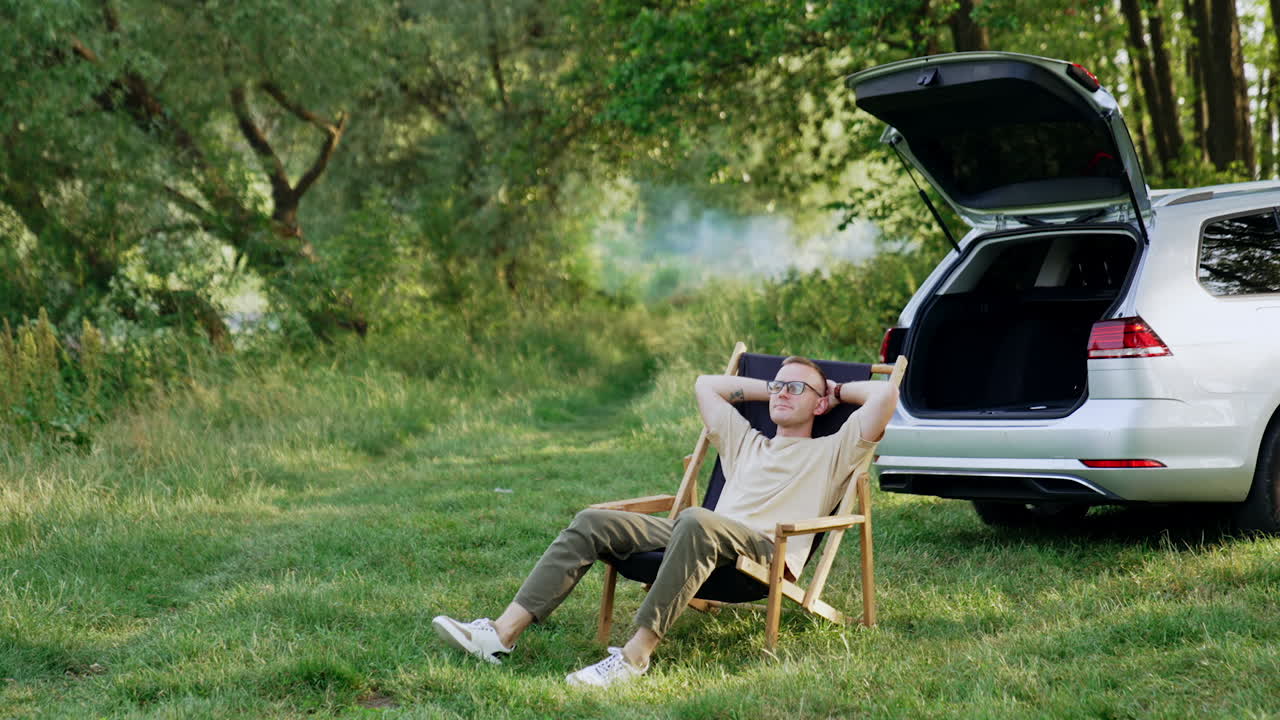 Man sitting comfortably in a folding chair stretches hands up. Summer relaxation in the wood.