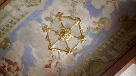 low shot of a golden chandelier in a historic building with ceiling painting