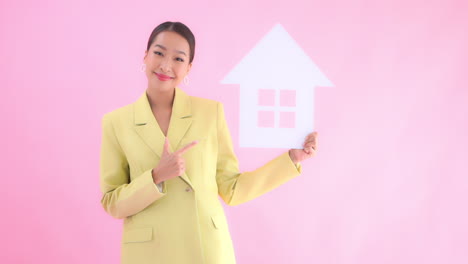 pretty female positive real estate agent holding up house symbol pink background