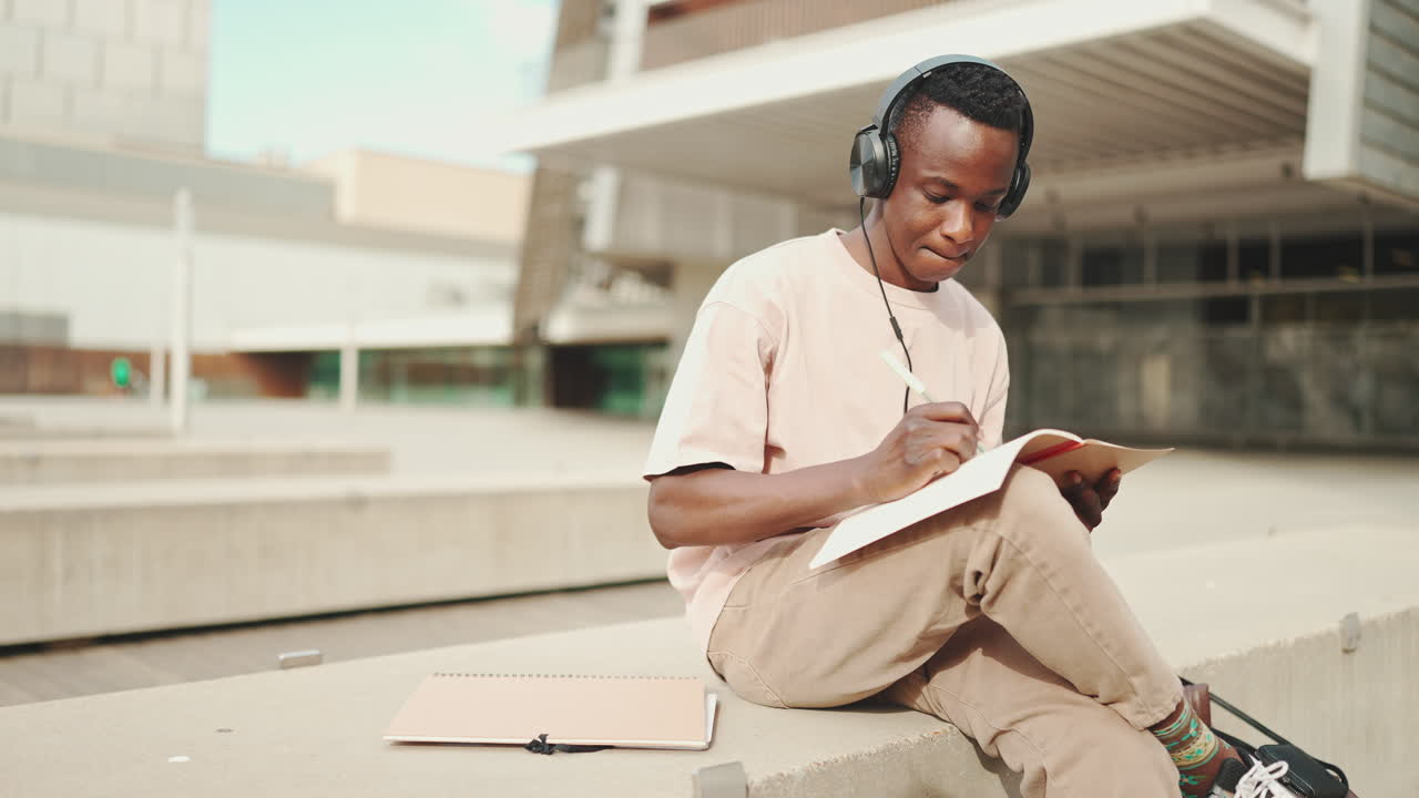 Homem com fones de ouvido escrevendo em um caderno ao ar livre