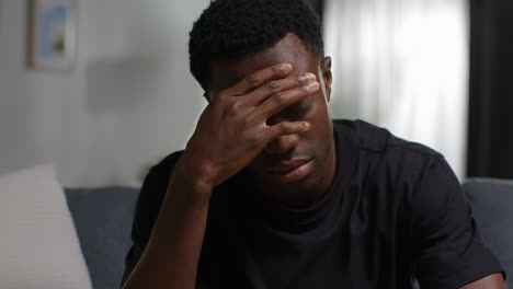 close up of unhappy and depressed young man sitting on sofa at home looking anxious and worried rubbing forehead 1