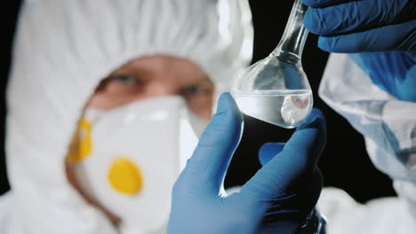 a man in a protective suit and a respirator examines a flask 2