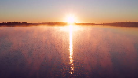 glorious sunrise over the freezing lake in new zealand with birds flying in the morning sky - wide drone shot