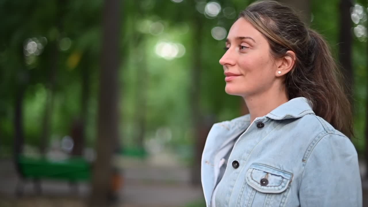 Donna mora con giacca di jeans che cammina in un parco alla luce del giorno