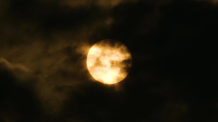 Radiant orange moon in night sky as dark clouds move