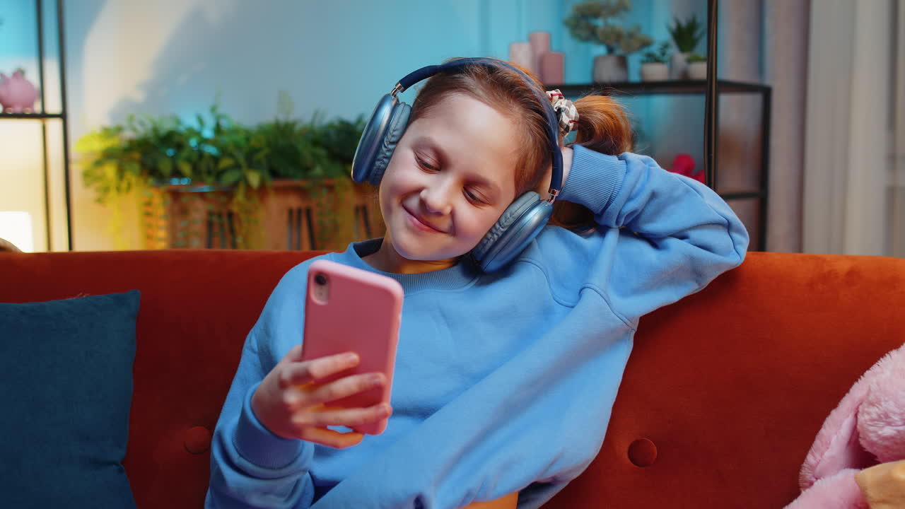niña feliz con auriculares inalámbricos relajándose sentada en el sofá en casa escuchando su música favorita