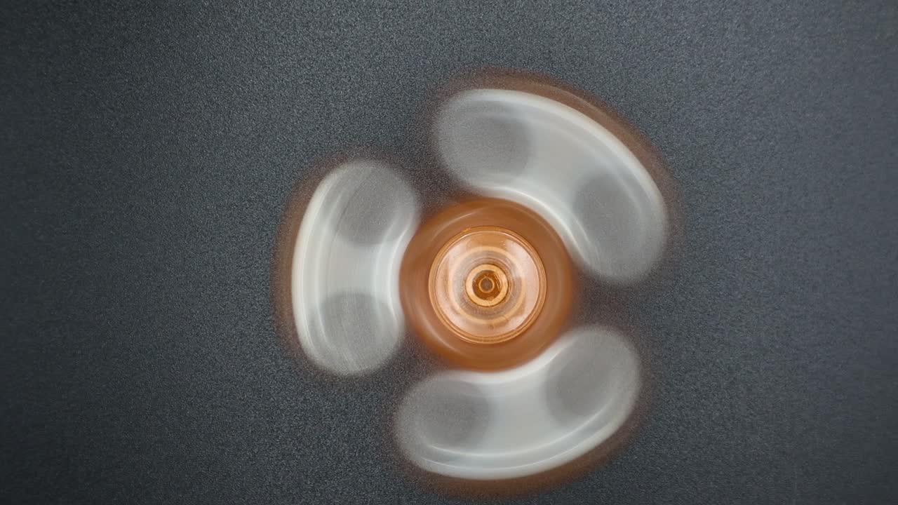 Orange fidget spinner toy in action on dark background, for a relaxation moment on a stressful day