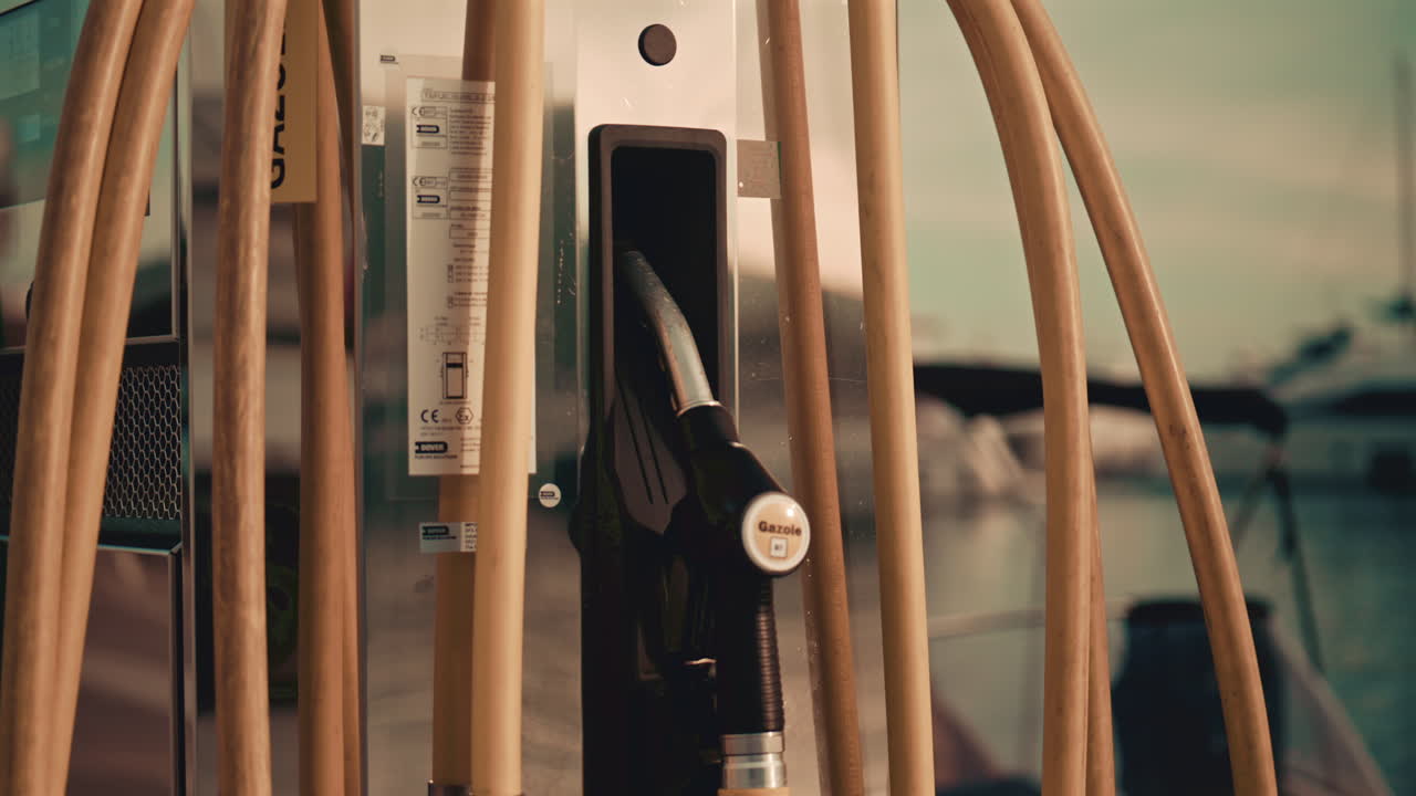Various hoses coloured in yellow, green, and blue, hang beside modern marina fuel pumps, boat at the fuel station