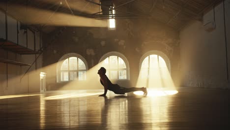 a man in a black summer sports uniform does a cat stretch pose in the sun room. the rays of the sun paint the hall in golden