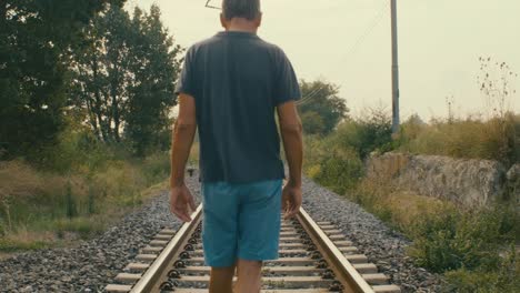 a man walks on the tracks of an abandoned station in the middle of nature in the countryside, reminiscing about the past when he played there with friends