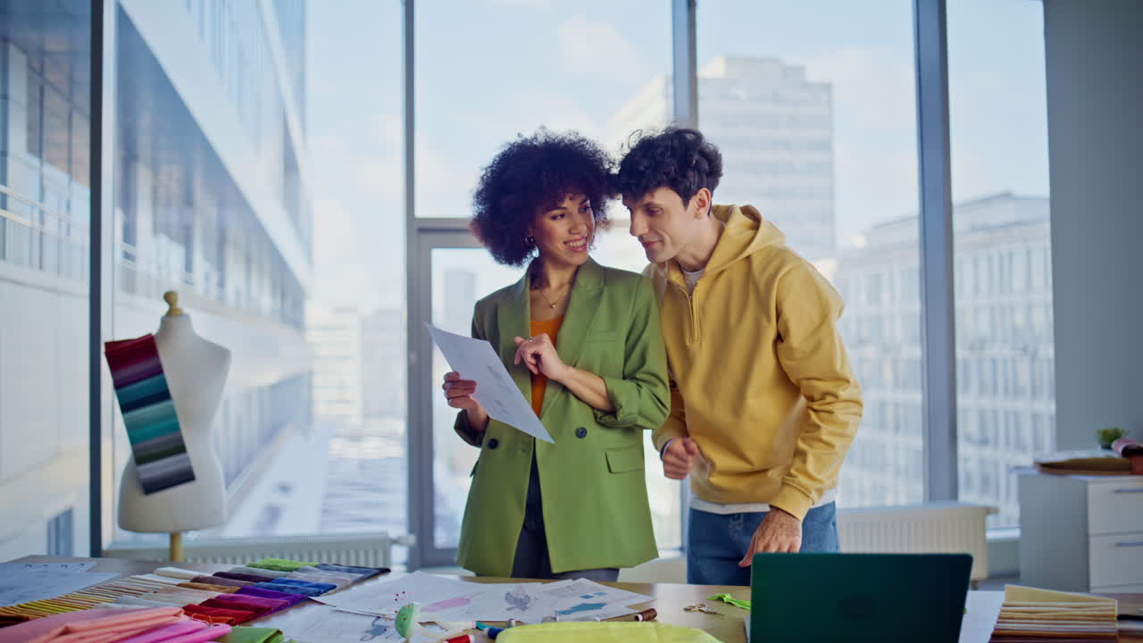 Apparel stylists creating clothing collection discussing sketches in agency