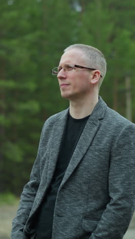 close-up view of a man in glasses and a gray jacket standing on a railway track, removed his glasses with one hand while looking thoughtfully into the distance, with a blurred background