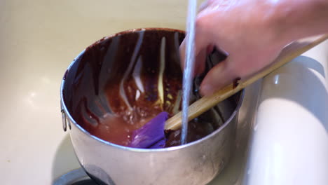 a chef cleaning up in the sink washing a mixing bowl and spatula that are covered in chocolate cake batter after baking