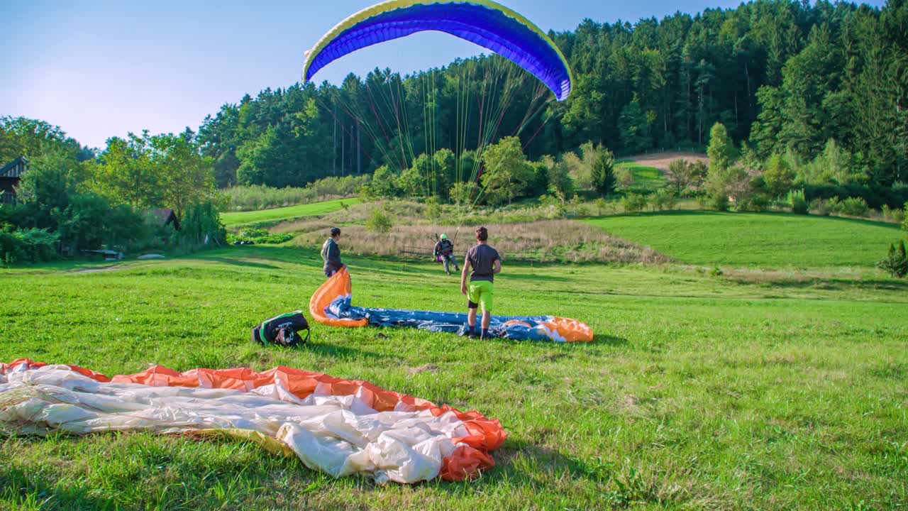 Paraglider pilot lands and falls on green grass, two Caucasian men watch, Padalci, slomo