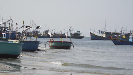 Many-fisherman-boats-moored-near-sandy-coastline-of-Vietnam,-handheld-shot
