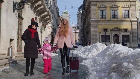 Sisters-tourists-travelers-walking-with-a-suitcase-on-snowy-city-street,-enjoying-time-together