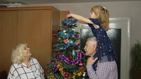 niña linda con abuelos mayores familia decorando árbol de navidad artificial en casa