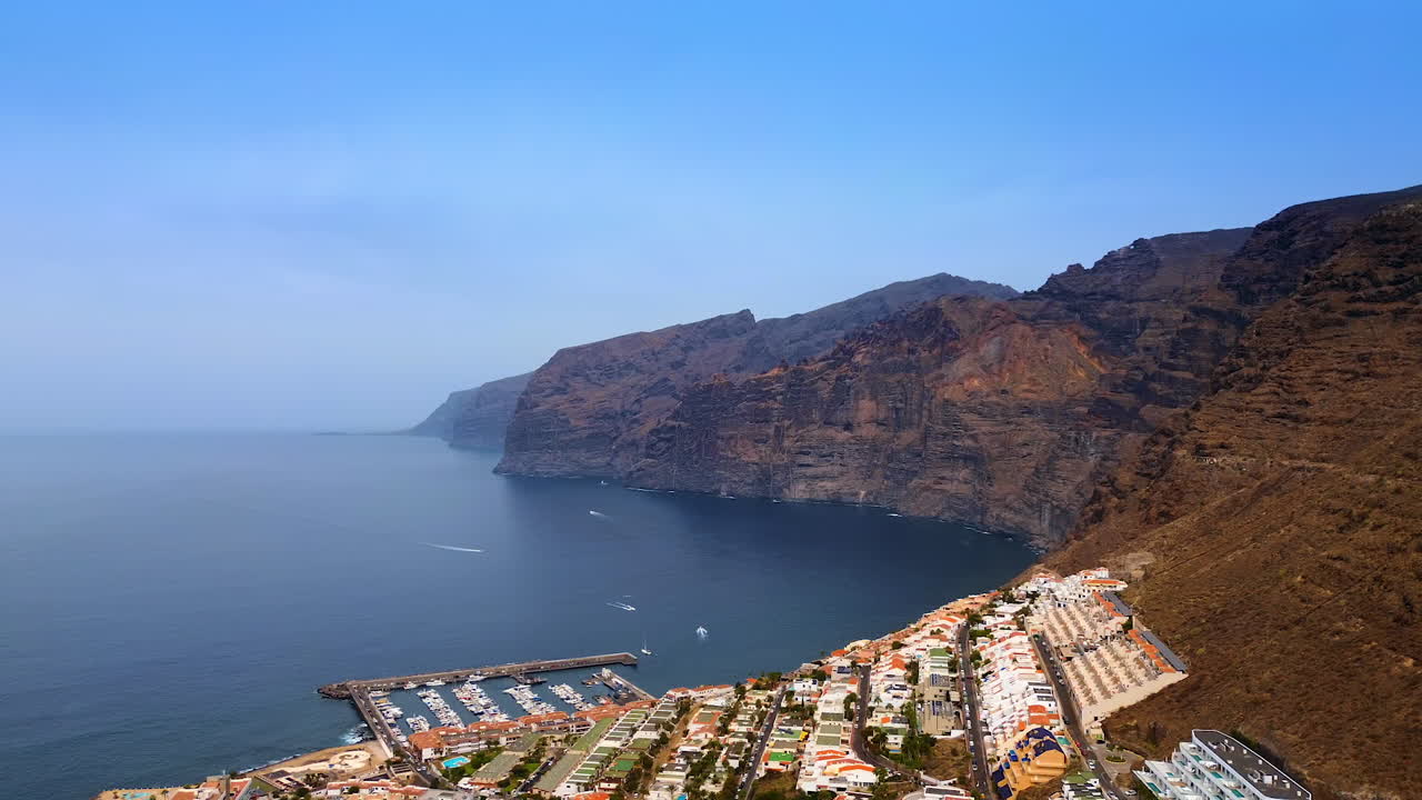 Rocce mozzafiato e inaccessibili con un'area urbana sul pendio. Alcuni yacht solcano le acque blu dell'Oceano Atlantico. Isola di Tenerife, Spagna. Vista aerea