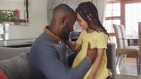 happy african american daughter and father embracing and talking on sofa