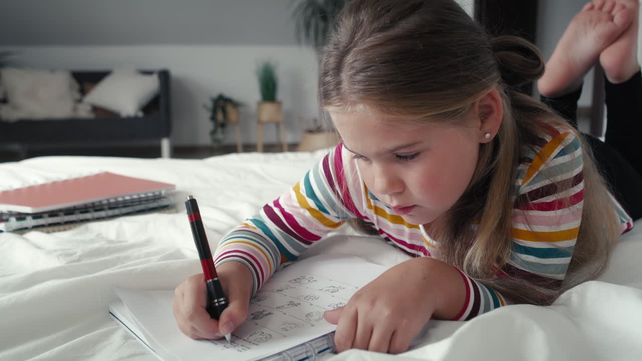 Elementary age girl studying while lying on front on the bed