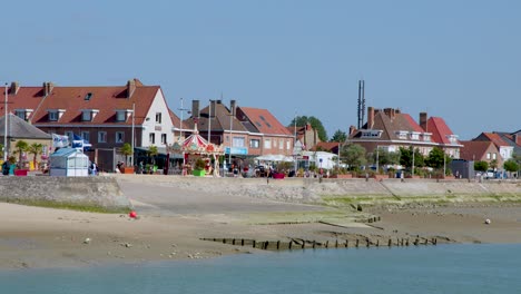 Wide shot slowly pans across seaside town, sandy beach, and calm water under clear daylight