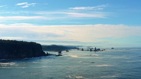 Stunning-aerial-drone-descending-shot-of-the-gorgeous-Third-Beach-in-Forks,-Washington-with-large-rock-formations,-cliffs,-small-waves-and-sea-foam-on-a-warm-sunny-summer-morning